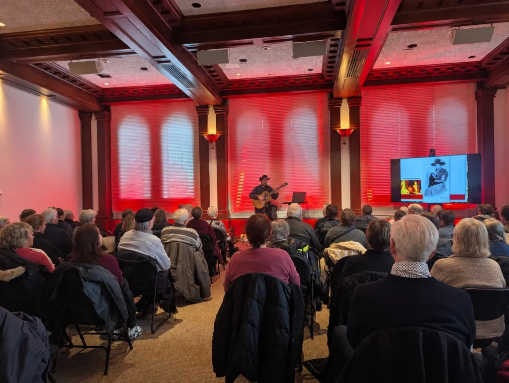 Sébastien Deshaies joue de la guitare devant un public lors d'une de ses conférences-concerts, dans une salle de spectacle.