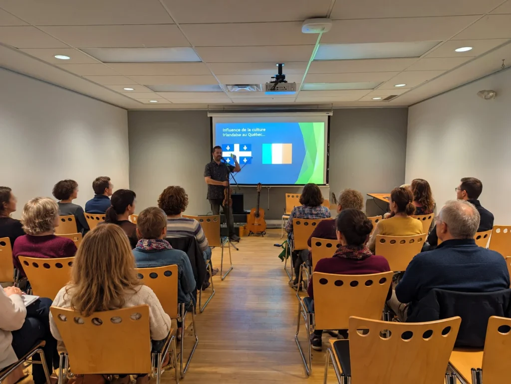 Sébastien Deshaies présente l'une de ses conférences-concerts sur la musique irlandaise devant un public, avec projection et instruments de musique.